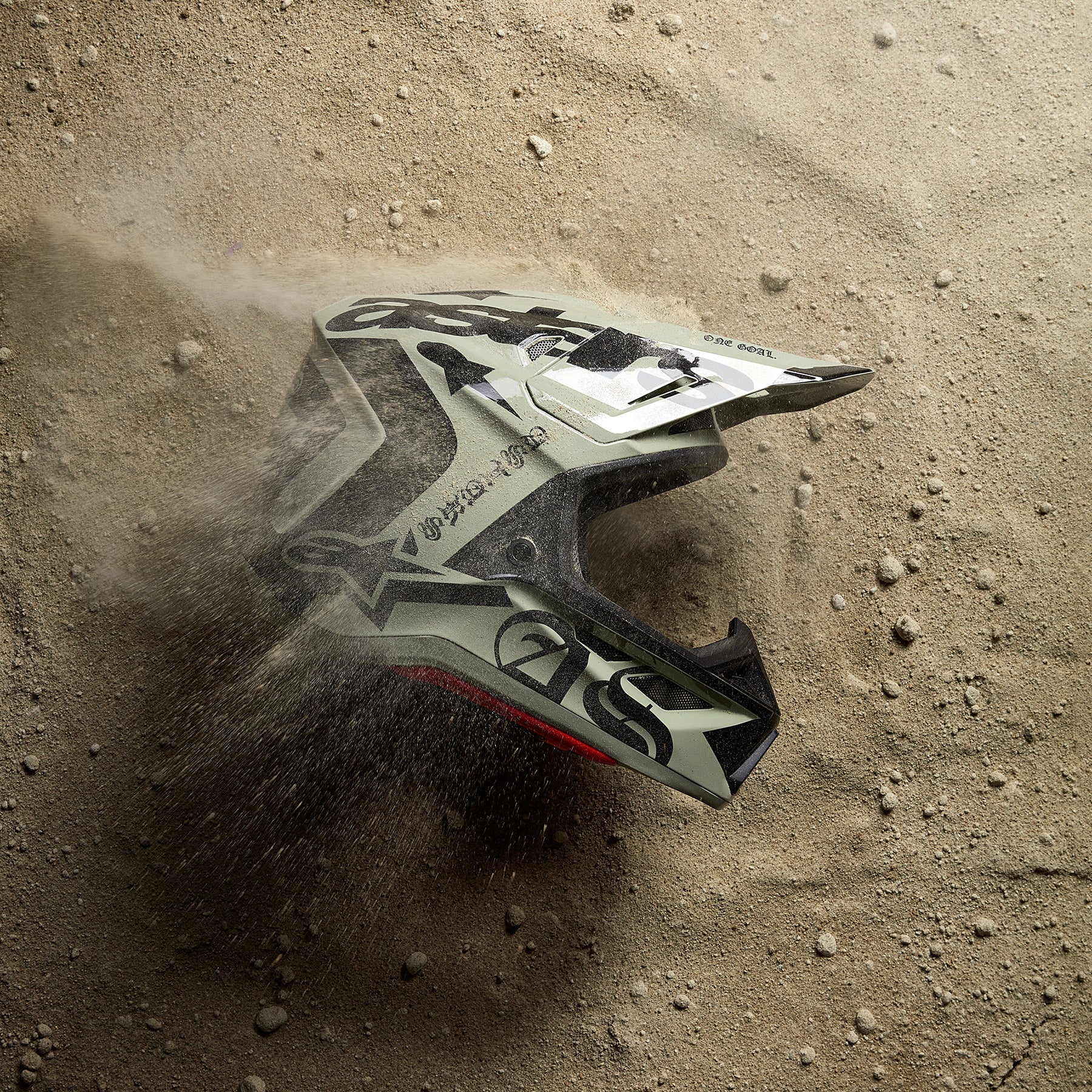 Alpinestars S-M7 Wolf Dust Helmet and Visor, Motocross protection in Dune Black, resting on desert sand with dust clouds.