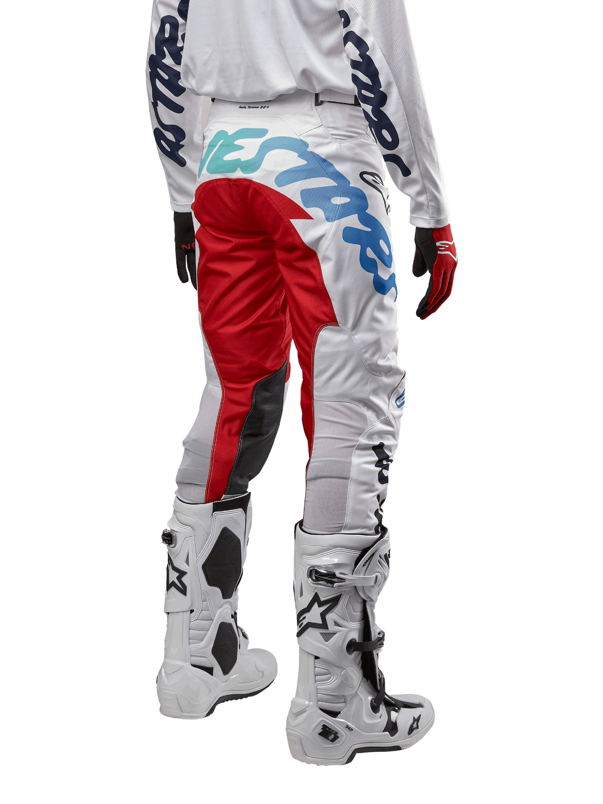 Alpinestars 2024 Racer Hana Hose, Motocross-Hose, Weiß Mehrfarbig mit roten und blauen Akzenten, Rückansicht mit großem Branding am Gesäß, getragen mit weiß-schwarzen Motocross-Stiefeln, entwickelt für Offroad-Performance und Langlebigkeit