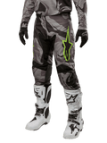Alpinestars 2024 Racer Tactical Hose, Motocross-Hose, Grau und Schwarz Tarnmuster, neongrünes Stern-Logo, getragen mit weiß-schwarzen Stiefeln und schwarzen Handschuhen, Geländefahrt-Ausrüstung