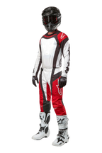 Motocross-Fahrer in kompletter Alpinestars-Ausrüstung, 2024 Techstar Ocuri Hose in Mars Rot Weiß Schwarz, passendes Trikot, schwarzer Helm mit Schutzbrille, schwarz-weiße Handschuhe und weiße Motocross-Stiefel, professionelles Offroad-Rennoutfit