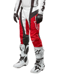 Alpinestars 2024 Techstar Ocuri Hose, Motocross-Rennsport-Hose, Mars-Rot, Weiß und Schwarz, getragen mit dazu passendem weiß-schwarzem Trikot, schwarzen Handschuhen und weißen Rennstiefeln mit Schnallen, technische Schutzausrüstung auf weißem Hintergrund