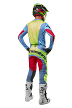 Motocross-Fahrer von hinten mit 2024 Techstar Ocuri Hose und passendem Trikot, Hellblau, Neongelb und Beerenrot, weiß-schwarze Stiefel, schwarzer Helm mit Neon-Akzenten, abgestimmte Alpinestars-Ausrüstung für Offroad-Rennen