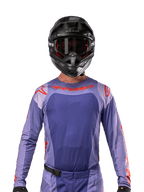 Alpinestars 2024 Techstar Ocuri Jersey, Lila und Hot Orange, getragen von einem Motocross-Fahrer mit schwarzem Helm und Goggles, mit lasergeschnittenen Perforationen auf der Brust, athletischer Rennpassform und auffälligem rotem Branding auf den Schultern und der Brust.