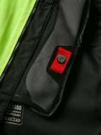 Alpinestars Tech-Air® 3 V2 System Detailansicht, Nahaufnahme der internen Netztasche mit roter Zuglasche und Druckknopf, leuchtend gelbes fluoreszierendes Panel, schwarze Textilkonstruktion mit Airbag-Modul-Etikett und Reißverschluss