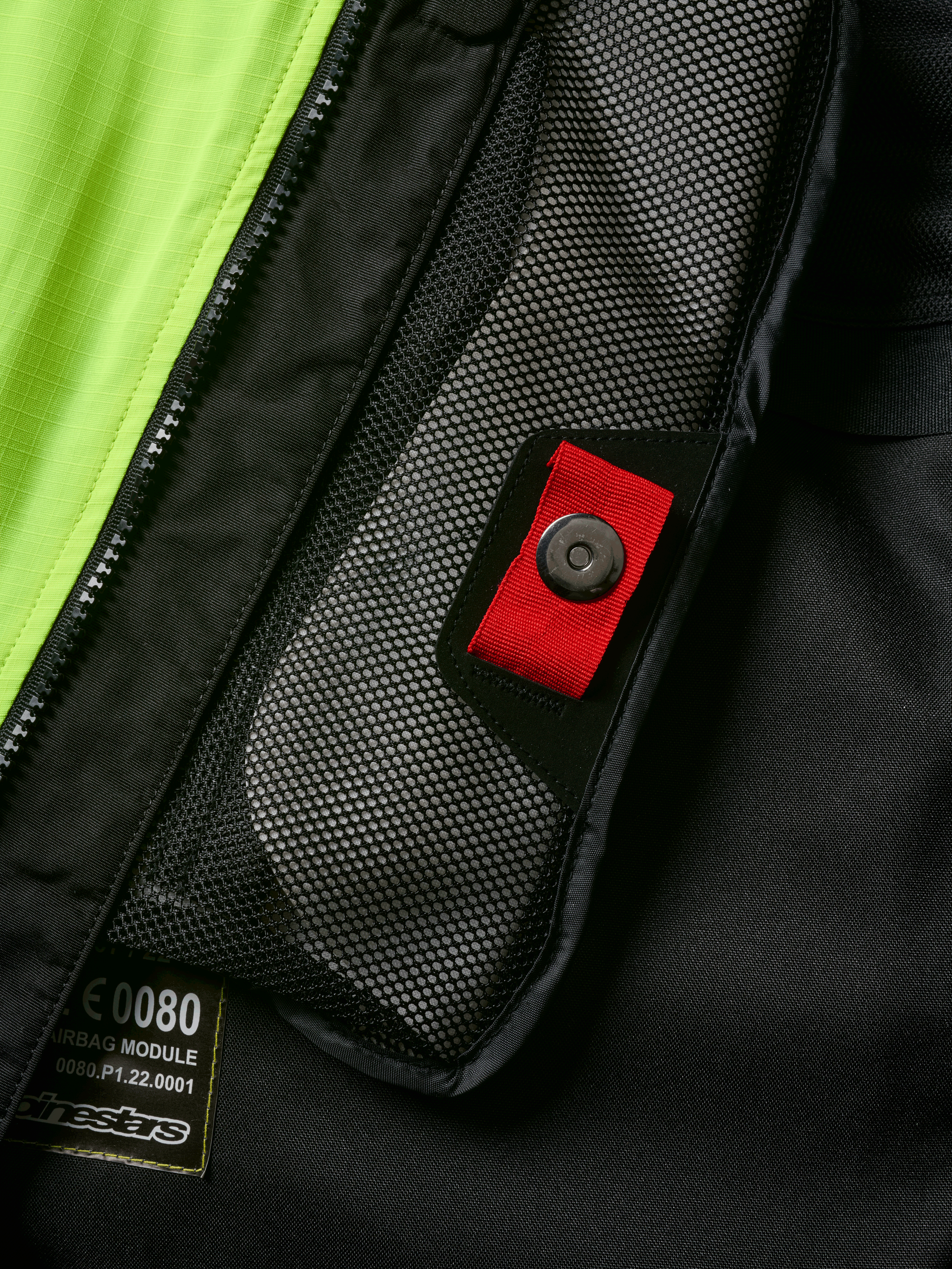 Alpinestars Tech-Air® 3 V2 System Detailansicht, Nahaufnahme der internen Netztasche mit roter Zuglasche und Druckknopf, leuchtend gelbes fluoreszierendes Panel, schwarze Textilkonstruktion mit Airbag-Modul-Etikett und Reißverschluss
