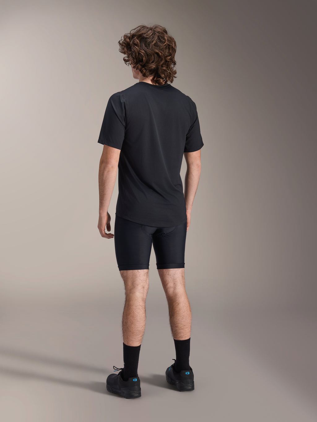 Alpinestars A-Dura Liner Shorts, schwarze Radsport-Innenhose, Rückansicht am Modell, eng anliegendes Stretchgewebe mit sichtbaren Sitzpolsternähten, kombiniert mit einem schwarzen T-Shirt und Radschuhen, Mountainbike-Bekleidung