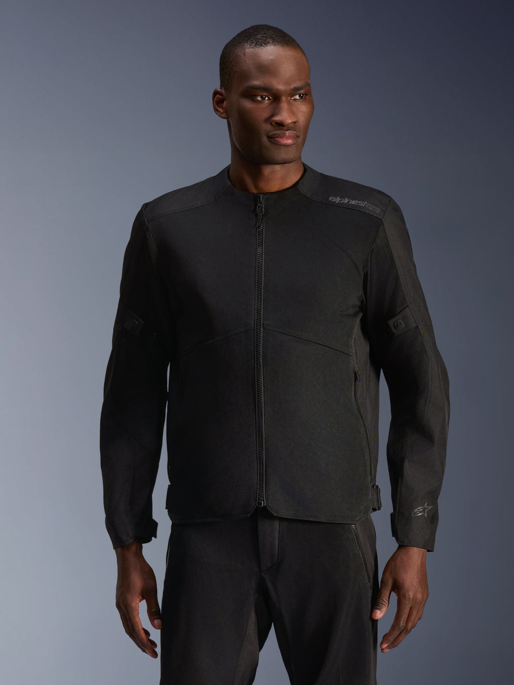 Männliches Model trägt die Alpinestars C-1 Air Jacke in Schwarz, moderne Motorradjacke mit großflächigen Tech-Mesh-Einsätzen und durchgehendem Frontreißverschluss, kombiniert mit passender schwarzer Motorradhose, urbane Lifestyle- und Pendler-Ästhetik