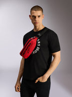 Alpinestars Only Linear Hüfttasche in Rot und Schwarz, quer über dem Körper über einem schwarzen Grafik-T-Shirt getragen, mit markantem schwarzem Alpinestars-Logo-Branding und verstellbarem Gurtbandriemen für einen urbanen, lässigen Look